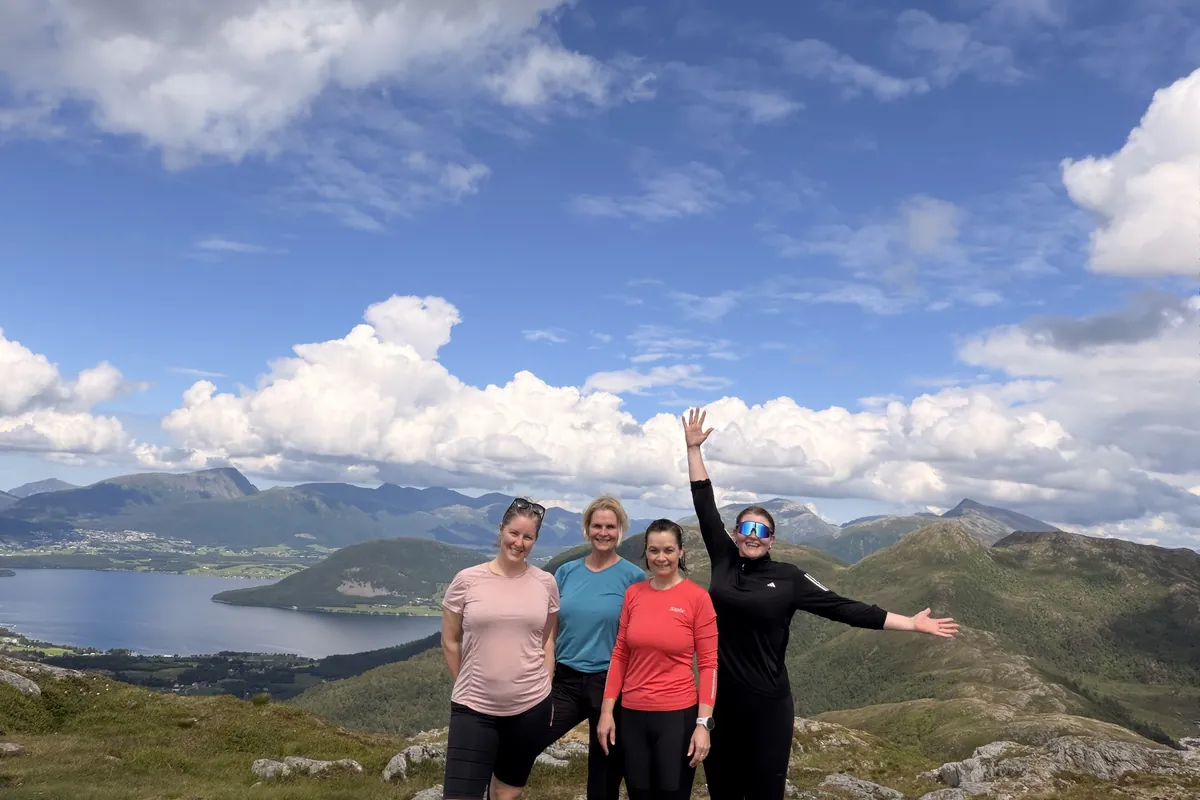 Fire turgåere på fjelltopp med utsikt over fjorden