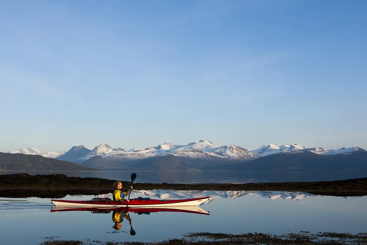 Kajakkpadler på blank fjord med snødekte fjell